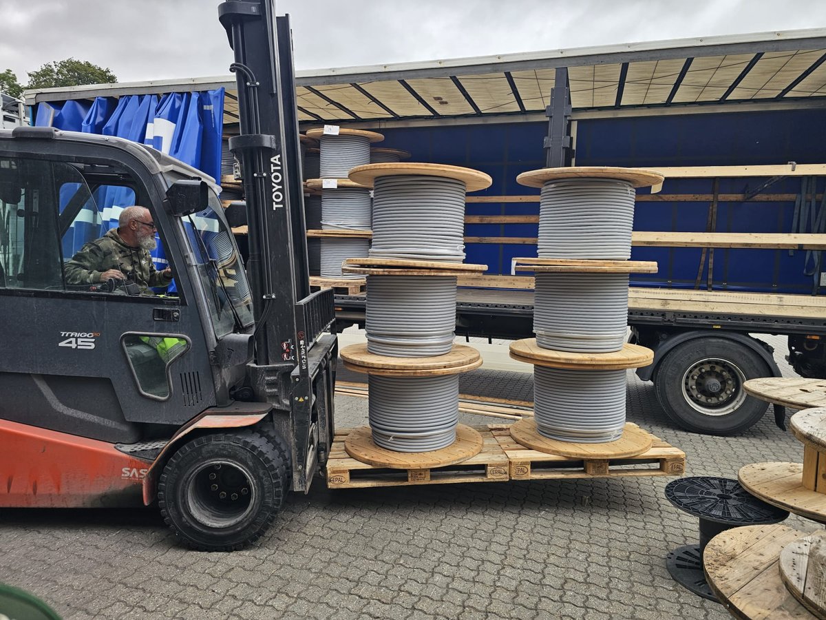 Cable reels being loaded alongside an open curtain trailer